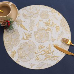 a place mat with gold flowers on it next to a cup of coffee and golden utensils