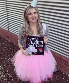 a woman in a pink tutu skirt holding up a sign that says thermo unicorn