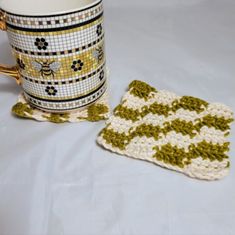 a coffee cup next to a crocheted coaster with a bee on it and a mug cozy