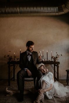 a bride and groom sitting on a chair in front of a table with lit candles