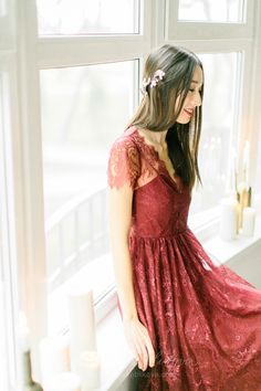 a woman standing in front of a window wearing a red lace dress with short sleeves