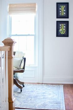 a living room with white walls and wooden floors, two framed pictures on the wall