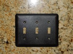 a black electrical outlet cover on a marble counter top with three holes in the middle