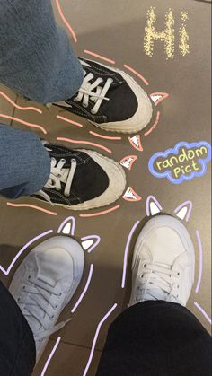 two people standing on top of a black and white skateboard with writing underneath them