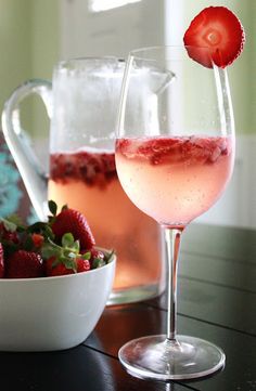 two wine glasses with strawberries in them on a table next to a pitcher of water