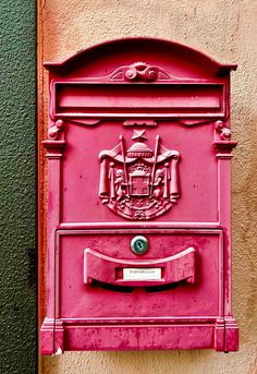 a pink mailbox mounted to the side of a building with a coat of arms on it