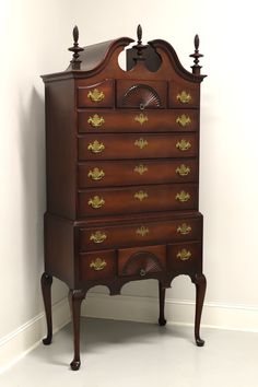 an antique chest of drawers with brass decorations on the top and bottom, against a white wall