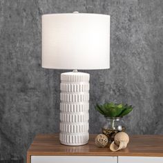 a white lamp sitting on top of a table next to a vase with a green plant