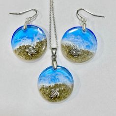 three pieces of jewelry on a white surface with sand and seaweed in the background