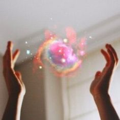 two hands are reaching up towards a colorful object in the air, with bright light coming from it