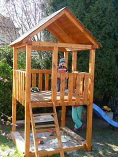 a child standing in front of a wooden play structure with a slide on the ground