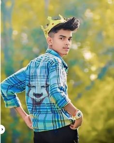 a young boy with a crown on his head standing in front of trees and looking at the camera