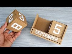 someone is holding two wooden blocks with the numbers 5 and 6 on them in front of a cardboard box