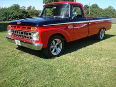 an old red and black truck is parked in the grass