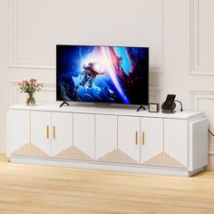 a flat screen tv sitting on top of a white entertainment center next to a vase with flowers