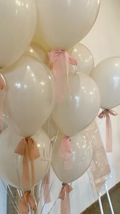 a bunch of white balloons with pink bows on them