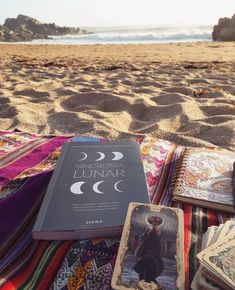 an open book sitting on top of a beach next to a pile of cards and blankets