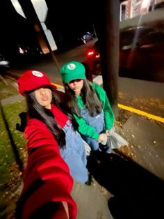 two young women sitting on the side of a road at night, one wearing a green hat