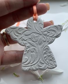 a hand holding a silver ornament with an orange ribbon around it's neck