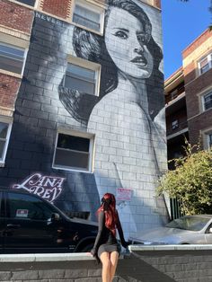 a woman standing in front of a building with a mural on it's side