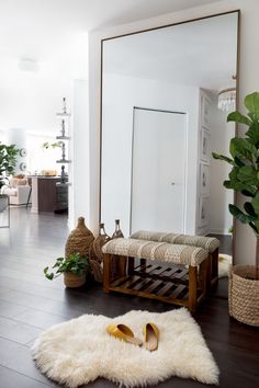 a large mirror sitting on top of a wooden floor next to a white rug and potted plants