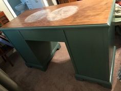 a green desk with a wooden top in a living room next to a chair and other furniture