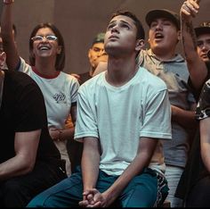 a group of young men sitting next to each other in front of a crowd with their hands up