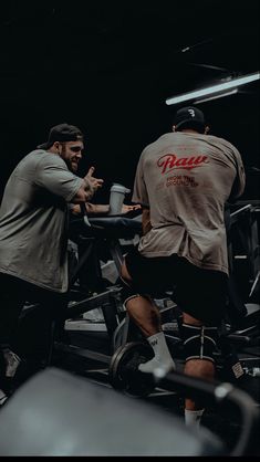 two men working out on exercise bikes in a dark room with no one around them