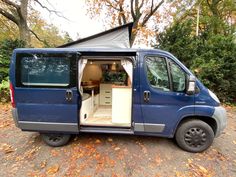 a blue van with its doors open on the side of a road in front of some trees