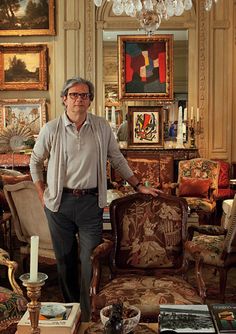 a man standing next to a chair in a living room filled with furniture and paintings