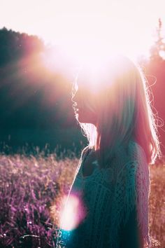 a woman standing in a field with the sun shining through her hair