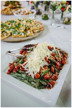 a white plate topped with asparagus covered in cheese next to other plates of food