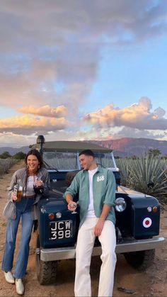 a man and woman sitting on the back of an old car in front of a desert landscape