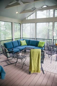 an outdoor living area with blue and green furniture on the deck, windows overlooking trees