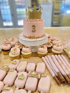 a table topped with lots of pink cupcakes next to a cake and cookies