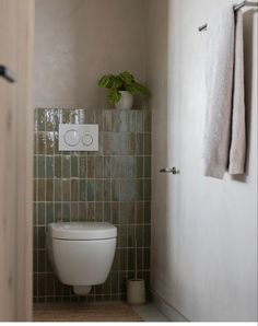 there is a toilet in the bathroom with green tiles on the wall and towel rack