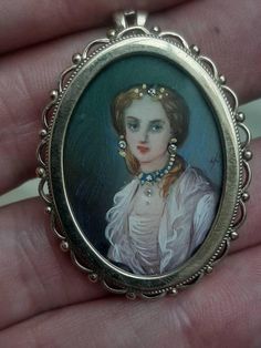 An antique diamond, gold, and enamel inlaid portrait, encased in a 9ct gold pendant brooch. The pendant brooch is Hallmarked 9ct gold. The reverse of the pendant, has a hinged bale whereby a chain can be placed through. It also has pin which can be locked in to place so that this piece can be worn both as a pendant and a brooch. When worn as a brooch the bale is hinged so can simply be folded down, and hidden from view. The length of this exquisite piece is 35 x 27mm's. The front of the pendant brooch contains the most beautiful, hand drawn, and hand coloured portrait of an elegant lady. Her face, along with her complexion really jump out at you. Her strawberry blonde hair is finely detailed and wraps around the reverse of her neck to the front highlighting the neckline. Along the neckline Antique Jeweled Pendant Brooches, Enamel Brooch Pendant Jewelry, Elegant Enamel Cameo Jewelry, Victorian Brooches With Locket Pendant, Elegant Miniature Jewelry For Collectors, Victorian Locket Pendant Brooches, Antique Pendant Brooches With Gemstone, Victorian Gold Enamel Brooch Pin, Antique Gold Gemstone Brooch