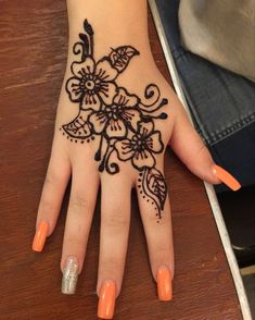 a woman's hand with an intricate hendi design on her left hand and orange nail polish