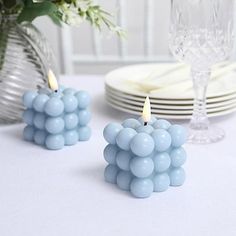 two blue candles sitting on top of a table next to plates and vase filled with flowers