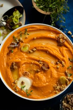 a white bowl filled with carrot soup and nuts on top of a blue table cloth