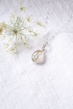 a small white flower sitting on top of a table next to a silver chain necklace