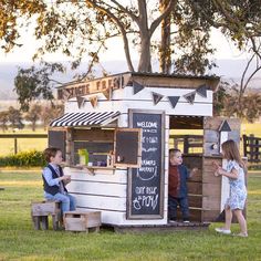 two children are playing outside in front of a small food stand that is made out of pallets