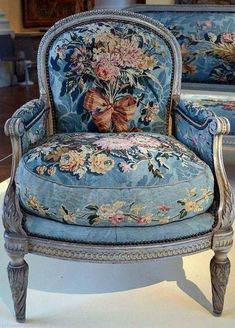 a blue chair with flowers on it sitting in front of a mirror and two other chairs