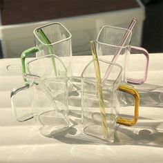 four different colored drinking glasses with straws in them sitting on a white tablecloth