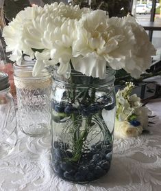 white flowers and blueberries in a mason jar on a table with lace doily