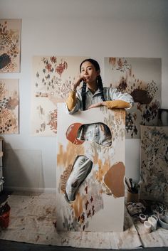 a woman sitting on top of a cardboard box in front of paintings and artwork behind her