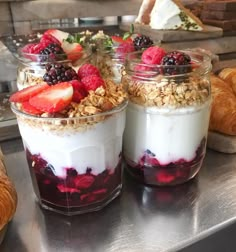 three desserts in glass jars with berries and yogurt on the top, along with croissants