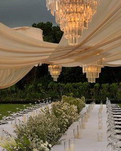 an outdoor wedding setup with chandeliers and white table cloth draped over the tables