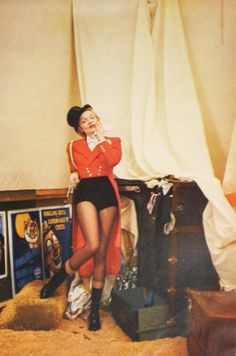 a woman standing in front of a pile of luggage talking on a cell phone while wearing an orange jacket