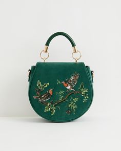 Key Features



Embroidered Elegance: Adorned with intricate embroidery depicting two facing robins on a branch, symbolizing luck, happiness, and rebirth.


Luxurious Velvet: Crafted from sumptuous fern green velvet, this saddle bag offers a rich texture and sophisticated appearance.


Functional Design: Designed for practicality with a rounded silhouette, top handle, and adjustable cross-body strap for easy carrying.


Secure Closure: Features a magnetic fastening to keep your essentials saf Fable England, Embroidered Accessories, Swan Jewelry, Velvet Bags, Embroidery Accessories, Luxury Christmas Gifts, Embroidered Handbag, Detailed Embroidery, Green Handbag